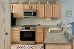 A kitchen with wooden cabinets, a stainless steel microwave, a gas stove, and a sink with a modern faucet. - Coastal Condo w/ Pool in South Padre Island! (South Padre Island)