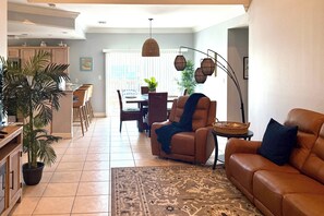 A living room with a brown leather sofa, a dining area with a table and chairs, and a kitchen with a counter and stools. - Coastal Condo w/ Pool in South Padre Island! (South Padre Island)