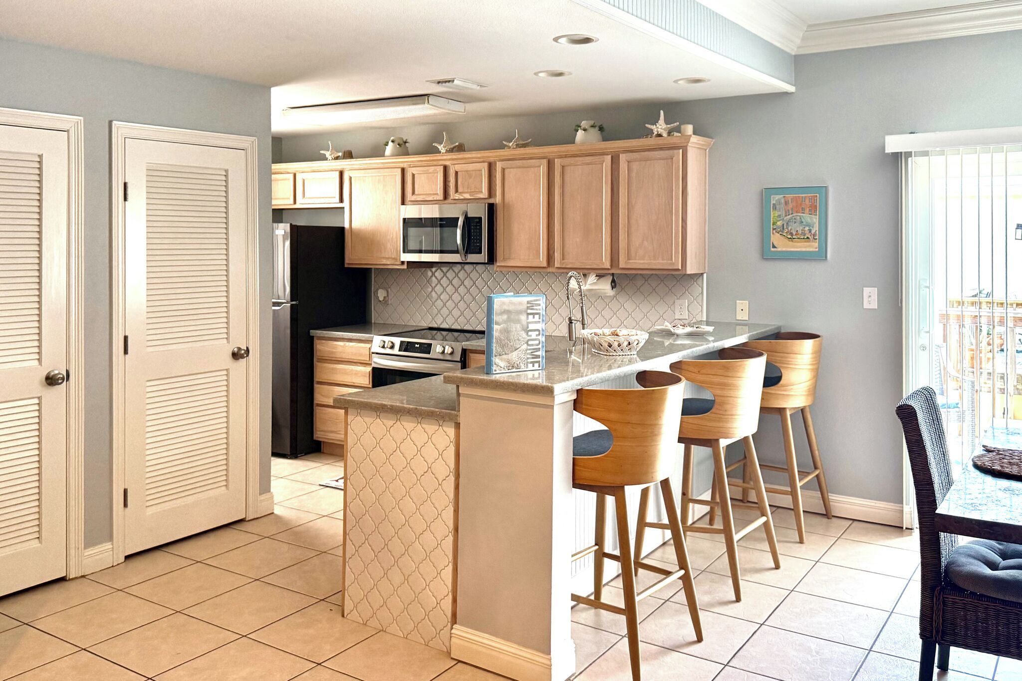 A modern kitchen with wooden cabinets, a central island with bar stools, and a microwave above the island.