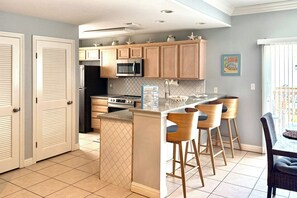 Una cocina moderna con armarios de madera, una isla central con taburetes altos y un microondas sobre la isla.