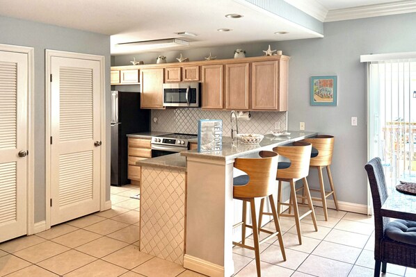 A modern kitchen with wooden cabinets, a central island with bar stools, and a microwave above the island.