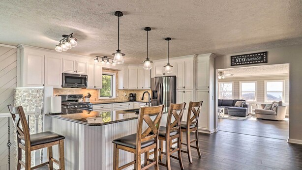 A spacious kitchen with white cabinets, a central island with bar stools, stainless steel appliances, and pendant lighting. - North Carolina Vacation Rental w/ Fire Pit & Grill (Leicester)