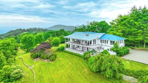 A large, two-story house with a blue roof, surrounded by lush greenery and a stone pathway. - North Carolina Vacation Rental w/ Fire Pit & Grill (Leicester)