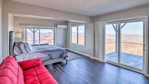 A bedroom with a large bed, a red couch, and a balcony with a mountain view. - North Carolina Vacation Rental w/ Fire Pit & Grill (Leicester)