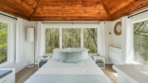 A bedroom with a wooden ceiling, large windows, a bed with white bedding, a bedside table, and a nightstand. - Family Friendly 5 Bedroom, Walk to Town, Beach & Ferry (Tisbury)