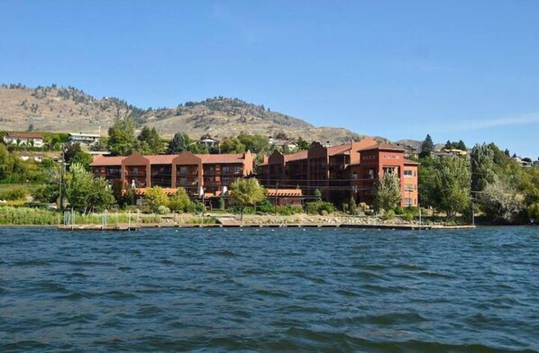 A hotel with multiple red-roofed buildings by a lake, surrounded by greenery and hills.