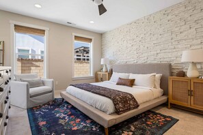 A bedroom with a large bed, a chair, a nightstand, and a window with a view of buildings. - No Bad Days 5 Bedroom Townhouse (St. George)