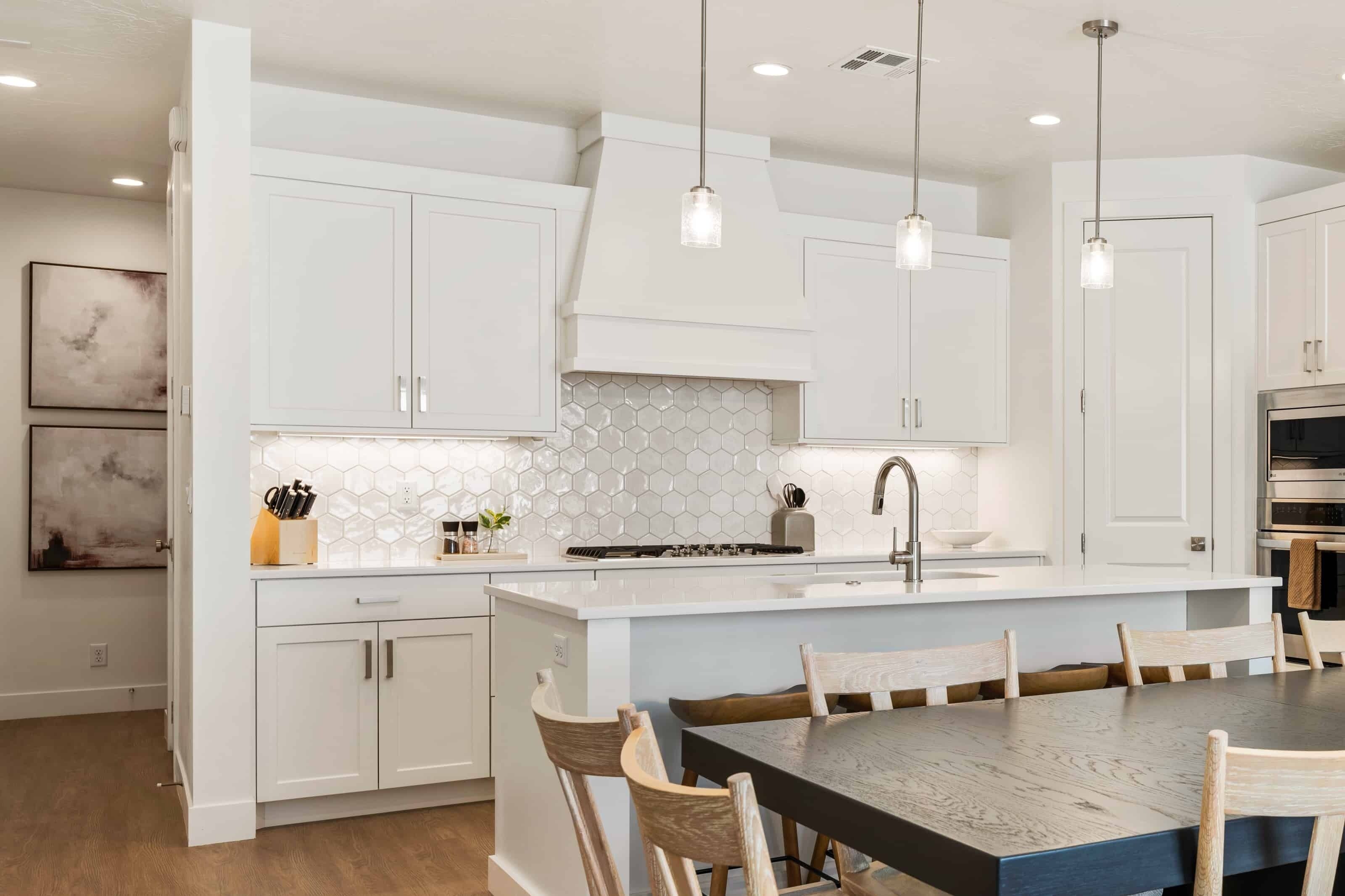 Une cuisine moderne avec des meubles blancs, un dosseret hexagonal et des luminaires suspendus.