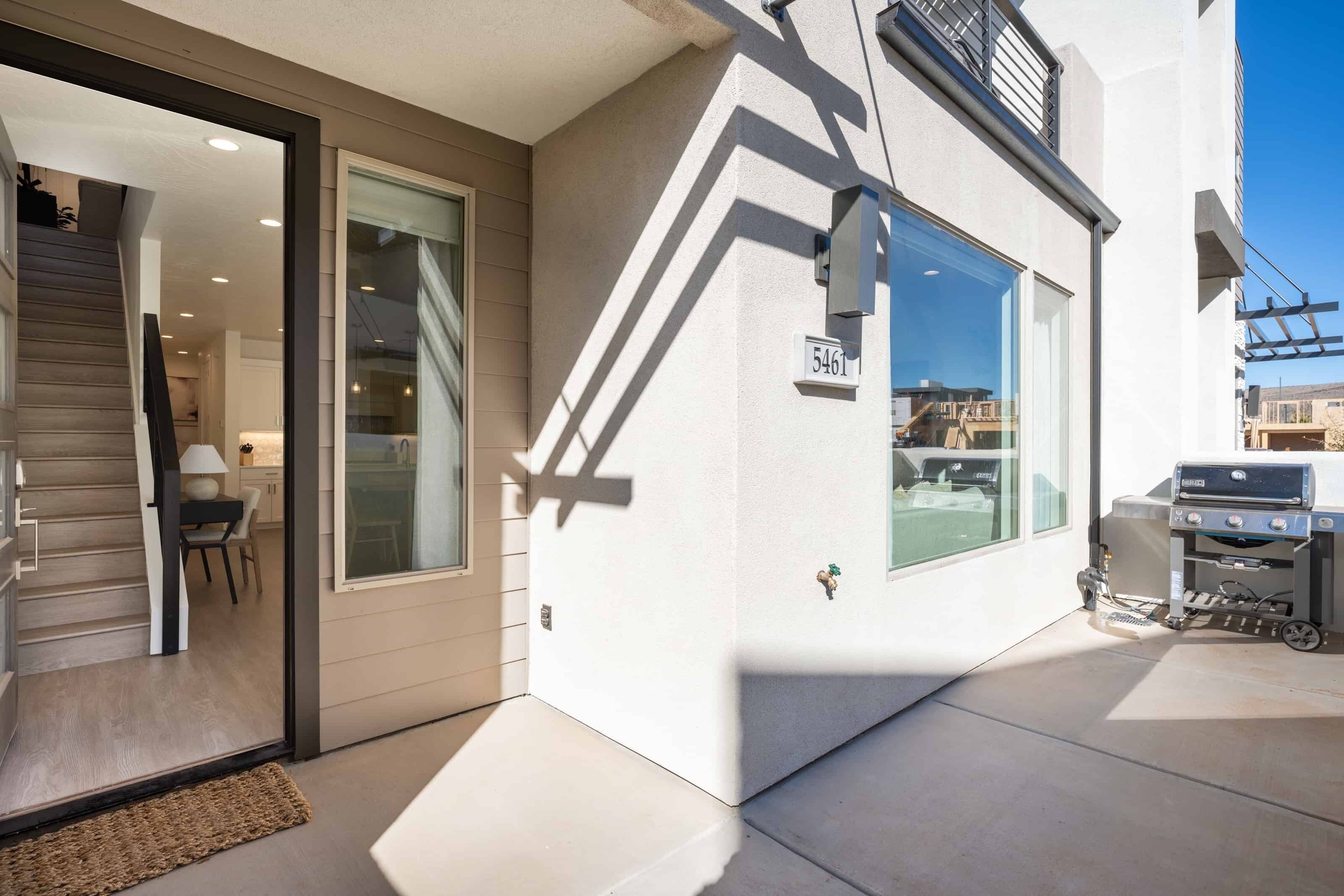 A modern building with a sliding glass door entrance, a patio area with a grill, and a clear view of the street.