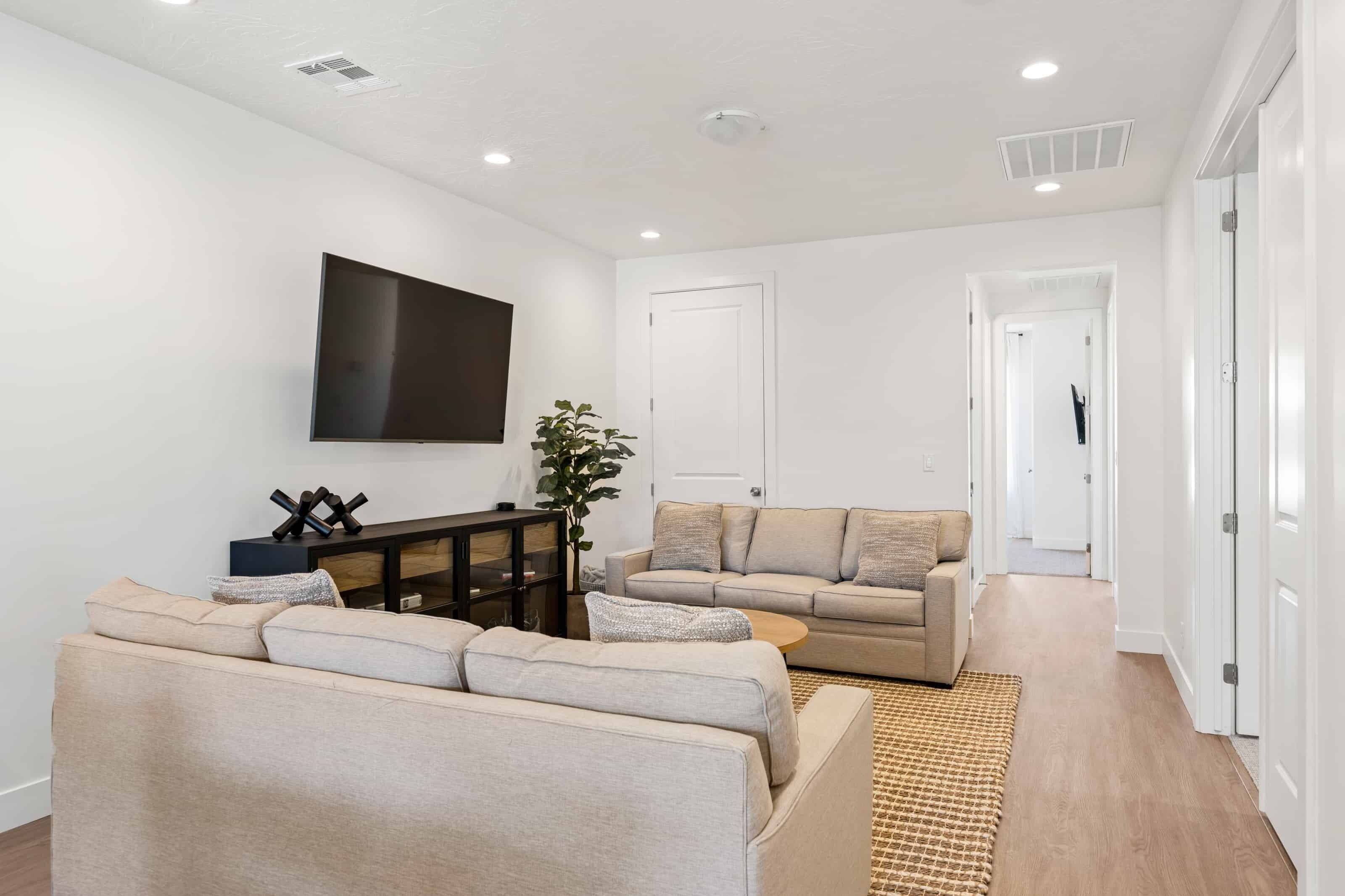 A modern living room with two sofas, a coffee table, and a flat-screen TV mounted on the wall.