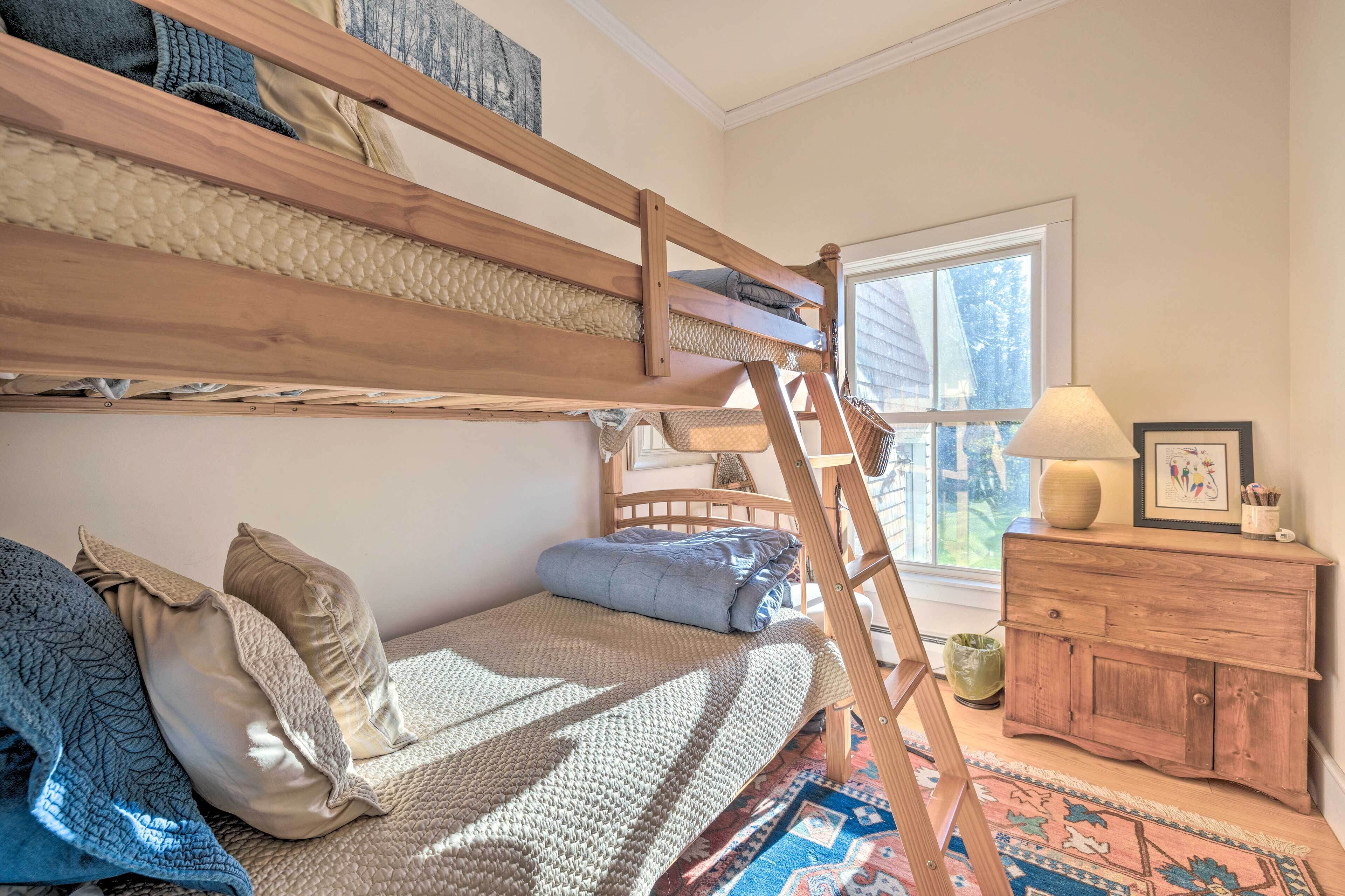 A bunk bed with a ladder, a wooden dresser, and a window with a view.