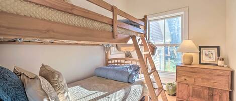 A bunk bed with a ladder, a wooden dresser, and a window with a view.