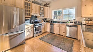 A modern kitchen with stainless steel appliances, wooden cabinets, and a large window providing natural light. - Private Home w/ Hot Tub Near Jay Peak Slopes (Montgomery Center)