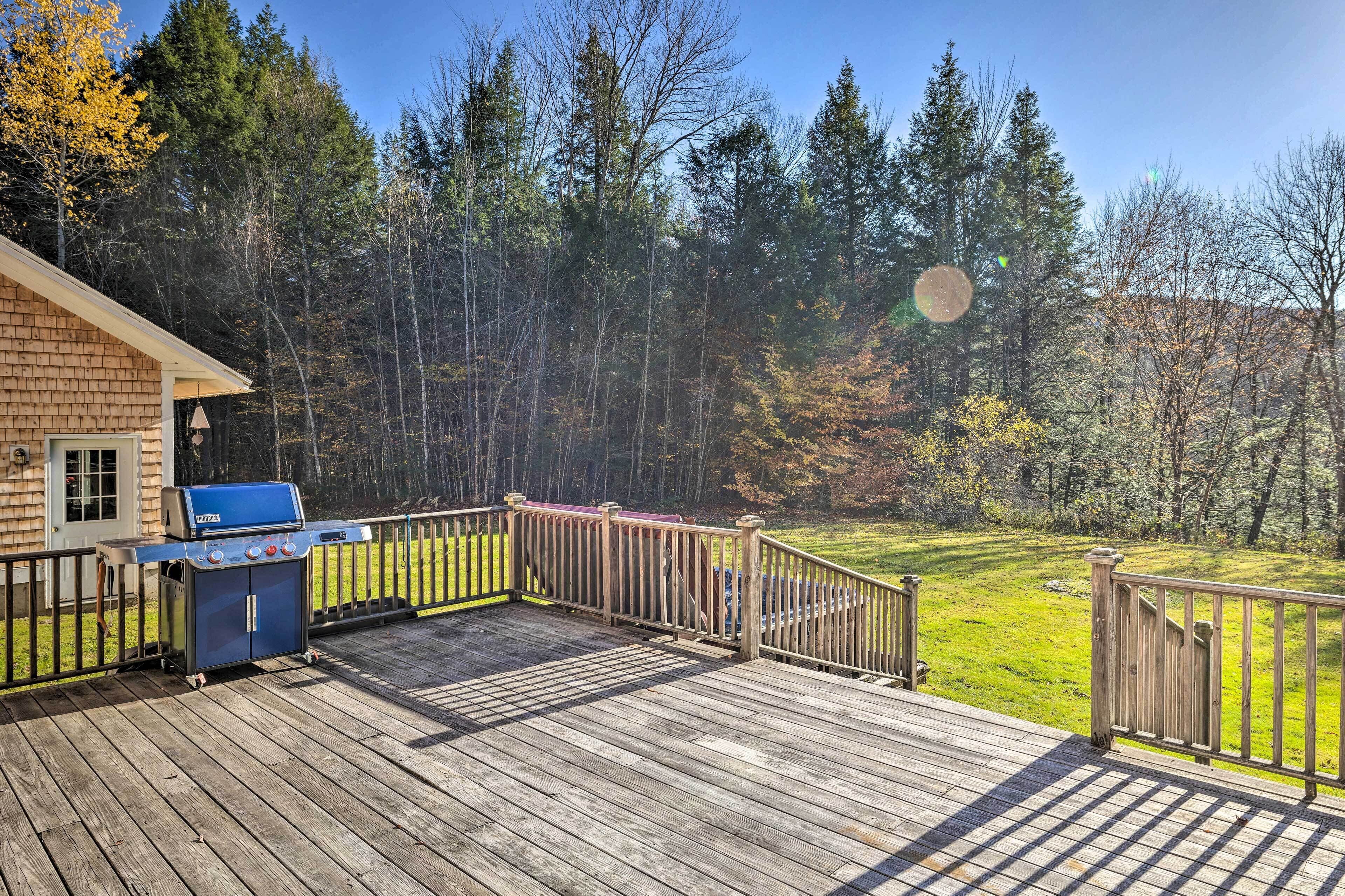 A wooden deck with a barbecue grill and a view of a forested area.