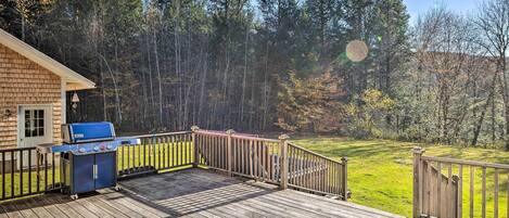 A wooden deck with a barbecue grill and a view of a forested area.