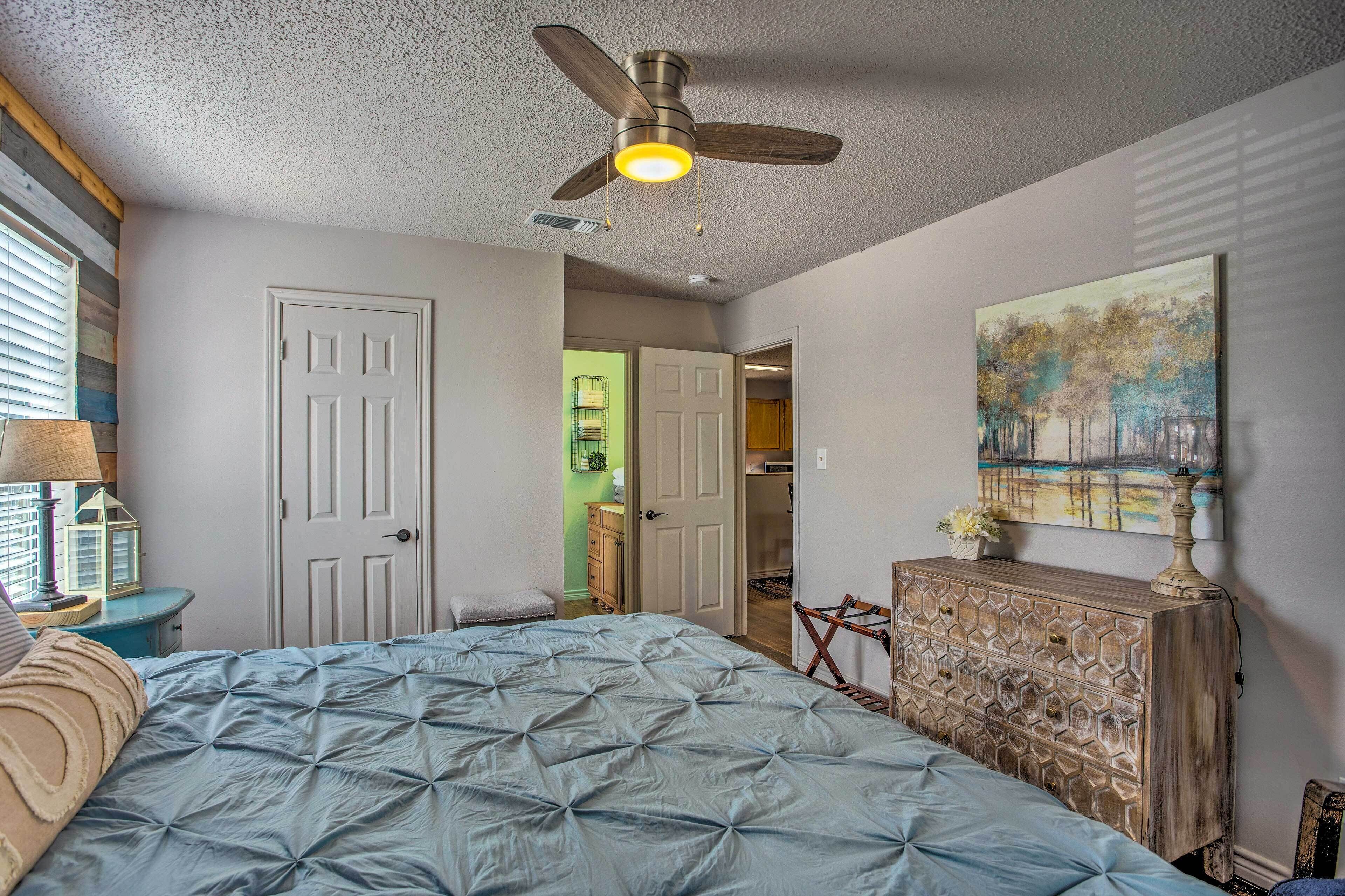 A bedroom with a bed, a ceiling fan, a dresser, and a painting on the wall.