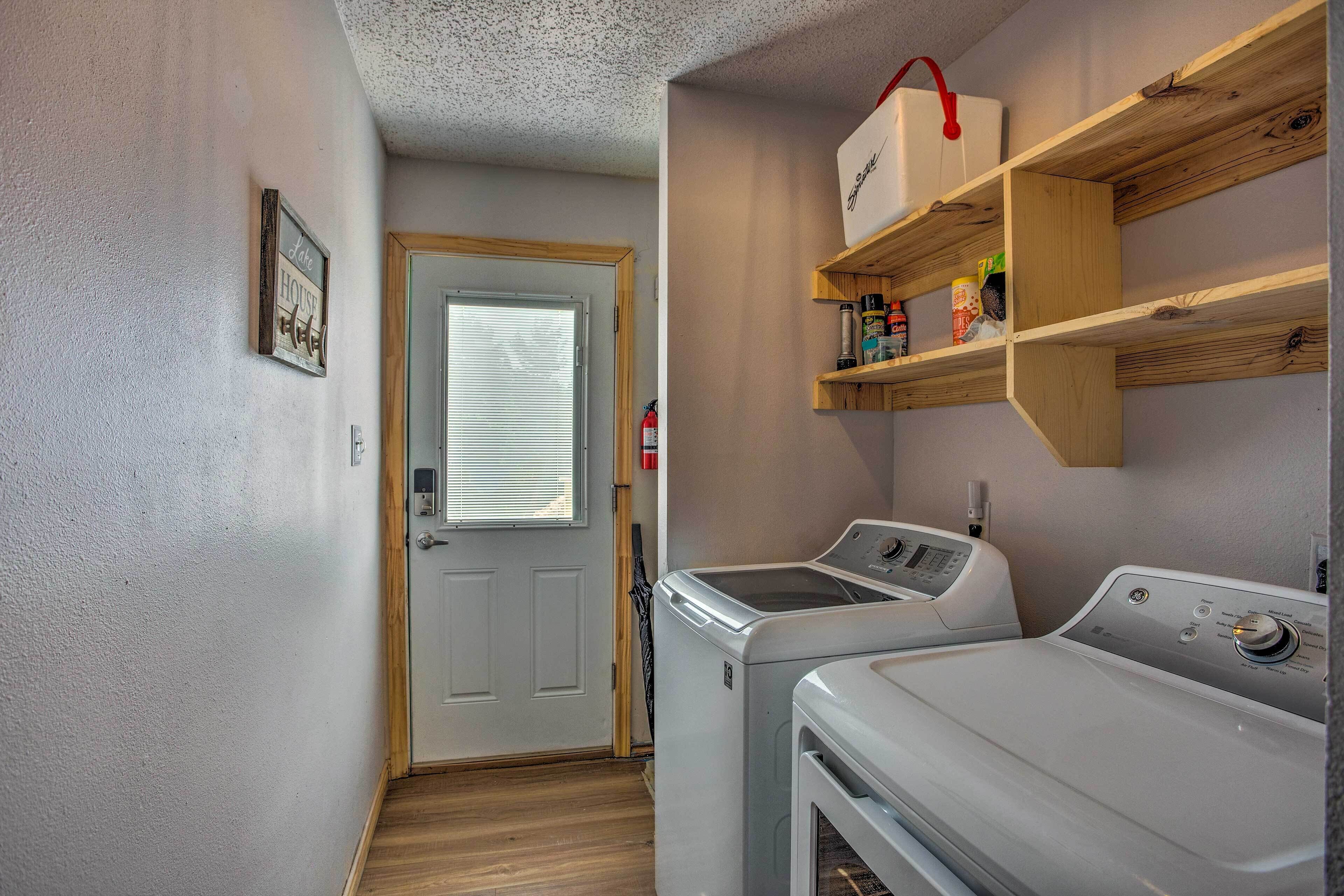 A laundry room with two washing machines, a wooden shelf with cleaning supplies, and a door with a window.