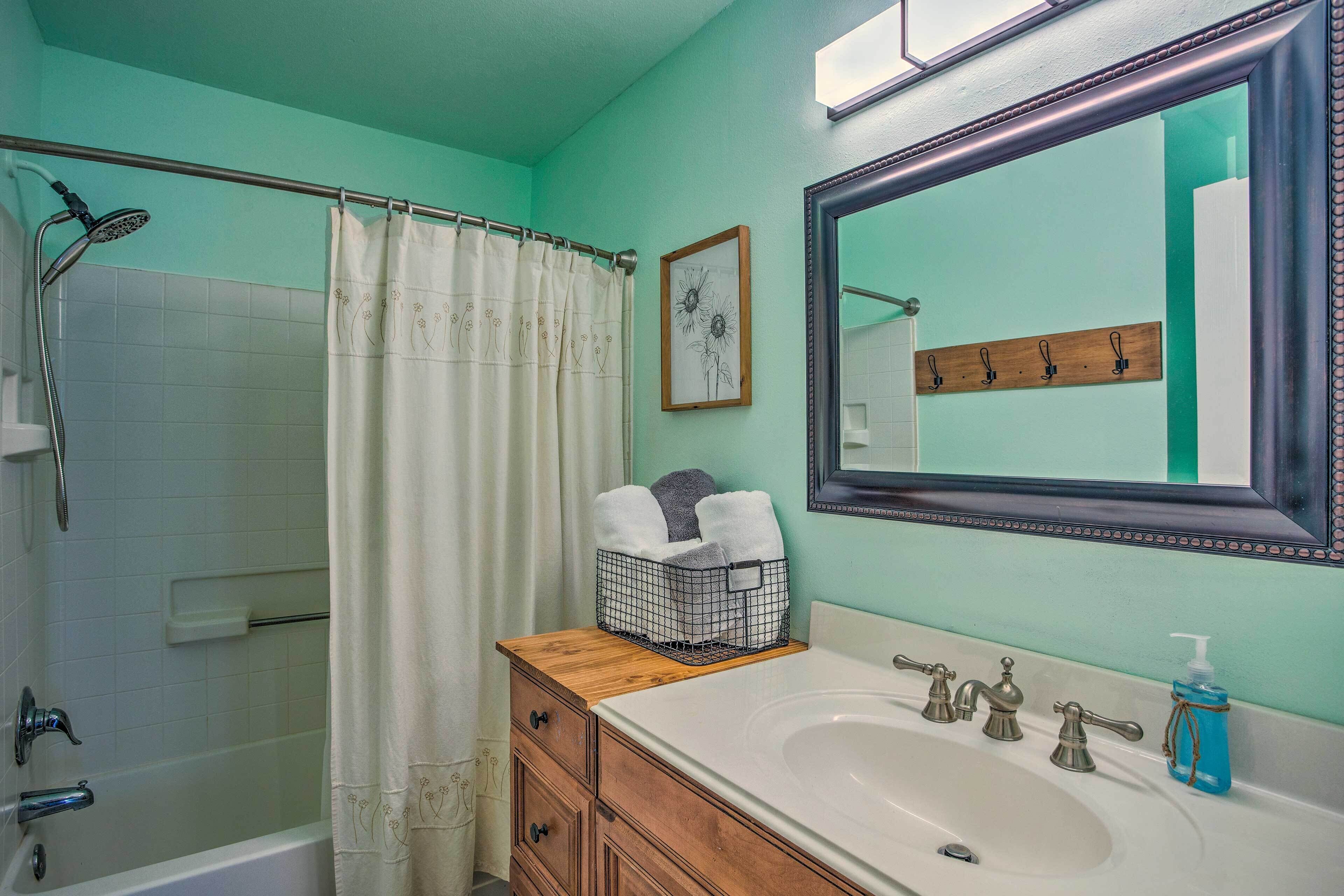 A bathroom with a bathtub, a shower, a sink with a mirror, and a towel rack.