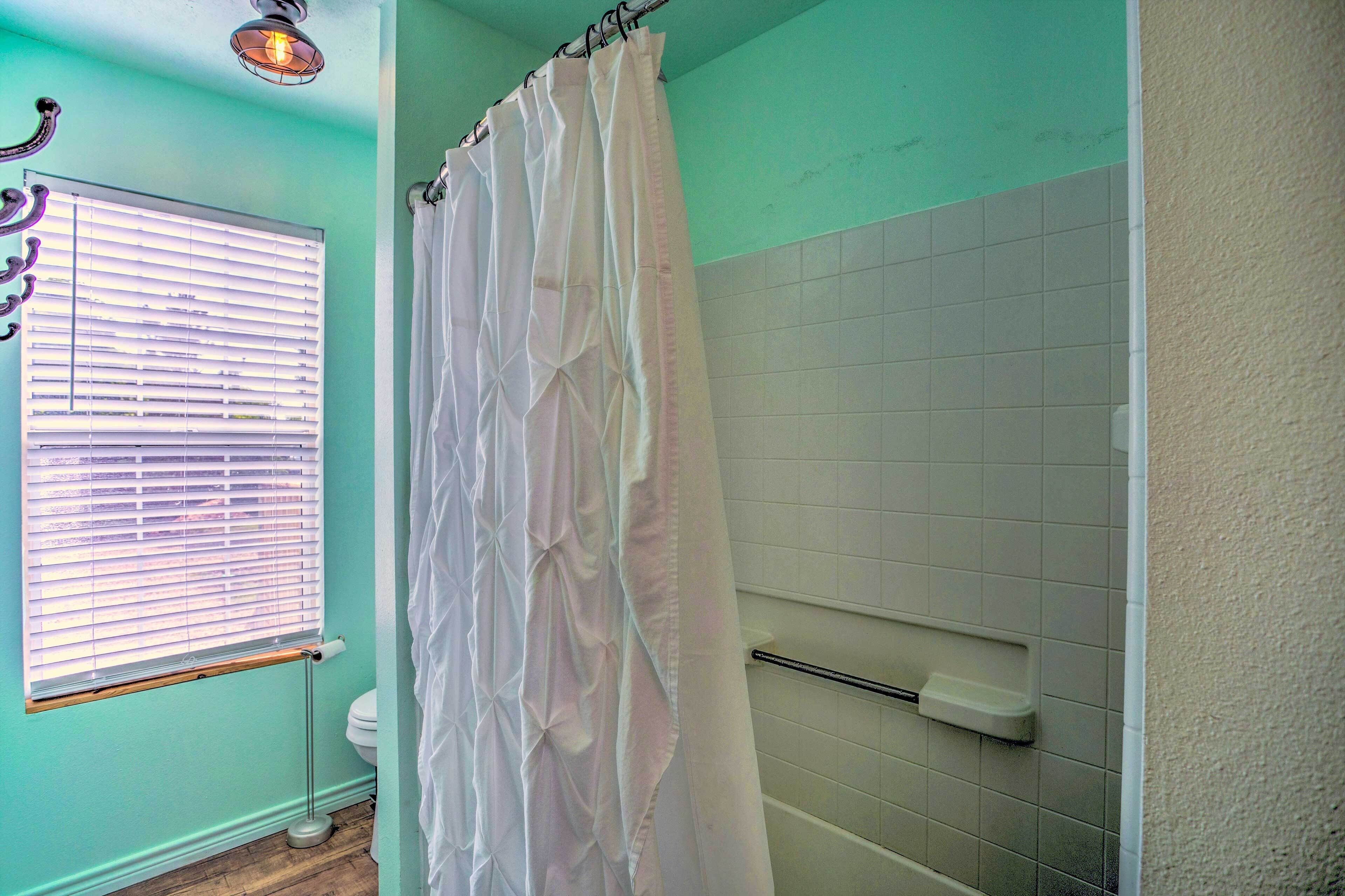 Een badkamer met douchegordijn, toilet, raam met zonwering en een handdoekhouder.