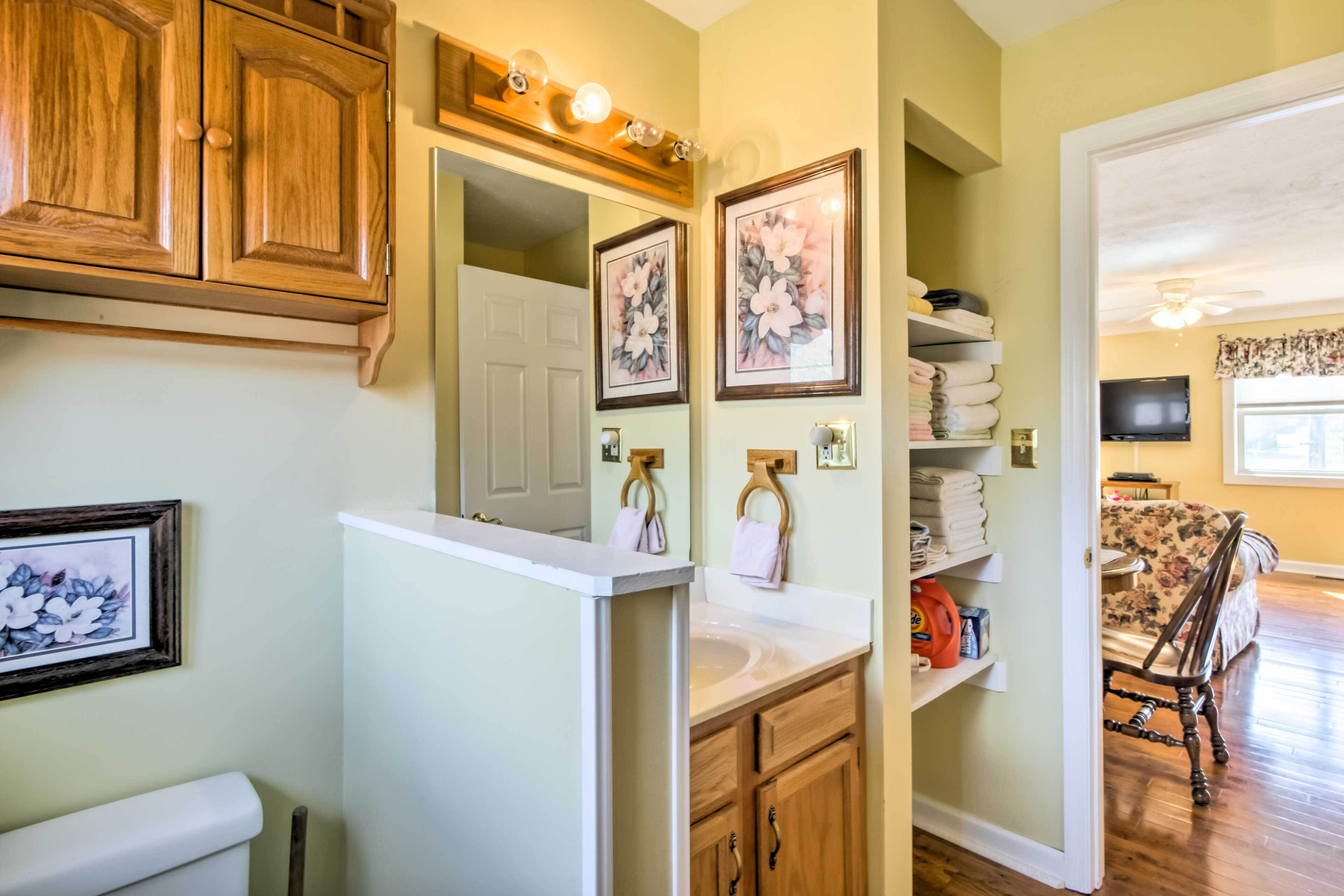 A bathroom with wooden cabinets, a white sink, and a mirror. There are framed floral pictures on the wall and a towel rack.