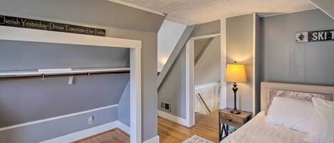 A bedroom with a bed, a nightstand, a lamp, a wall-mounted shelf, and a staircase.