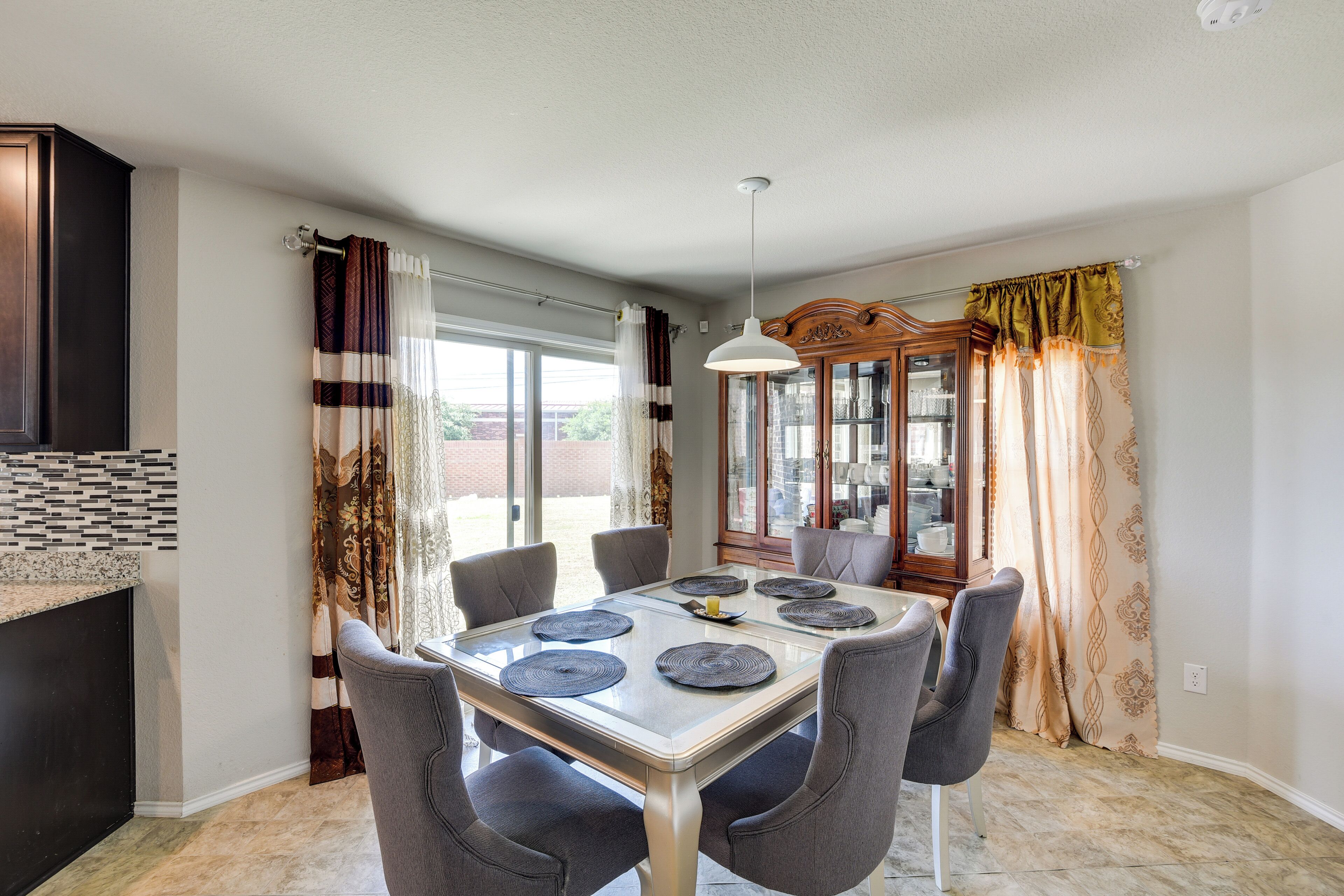 A dining area with a glass table, six chairs, and a chandelier.
