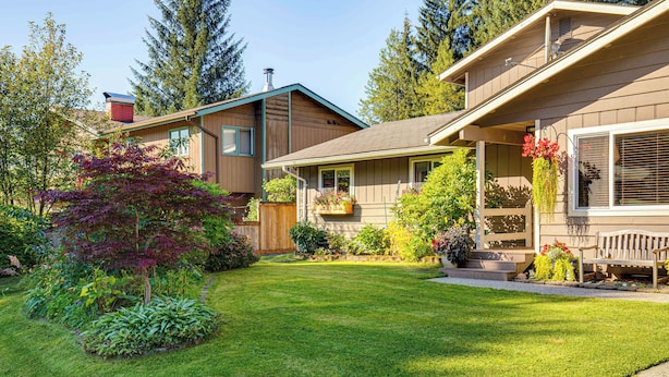 Ein Wohnhaus mit gepflegtem Rasen, einer Holzterrasse und einer Veranda mit einer Bank.