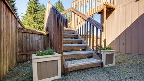 Eine Holztreppe mit Geländer führt zu einer Terrassenfläche, umgeben von Holzwänden und einem Kiesweg.