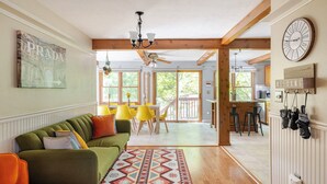 Un vaste espace de vie agrémenté d’un canapé vert, de fauteuils jaunes, d’un tapis à motifs et d’un ventilateur de plafond.