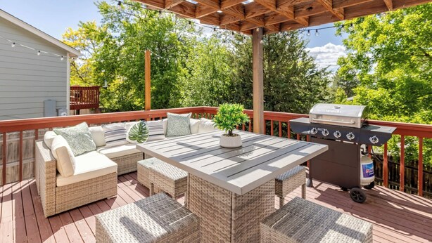 Une terrasse extérieure couverte, aménagée avec des meubles en osier, un barbecue et une plante en pot.