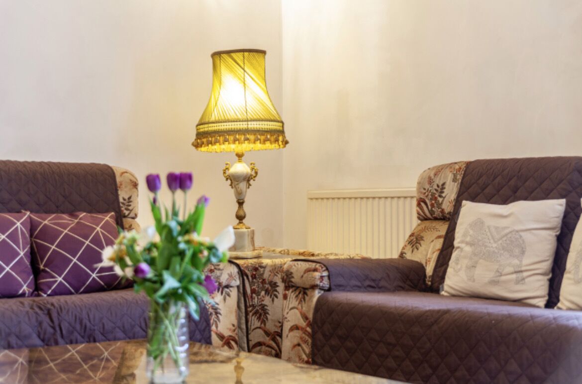 Ein Wohnzimmer mit zwei Sofas, einem Tisch mit Lampe und einer Vase mit Blumen.