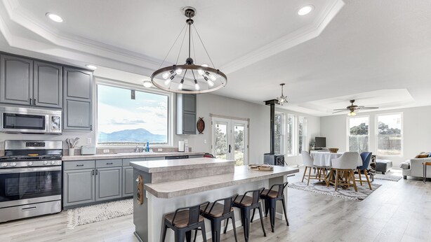 A modern kitchen with grey cabinets, a large island with bar stools, and a view of mountains through the windows. - Sauna & Views: Southern Colorado Vacation Rental! (Walsenburg)