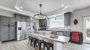 A modern kitchen with grey cabinets, stainless steel appliances, a central island with bar stools, and a large window offering a view. - Sauna & Views: Southern Colorado Vacation Rental! (Walsenburg)