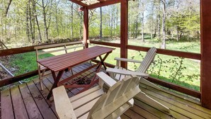 Een houten terras met een picknicktafel en twee Adirondack stoelen, met uitzicht op een bebost gebied.