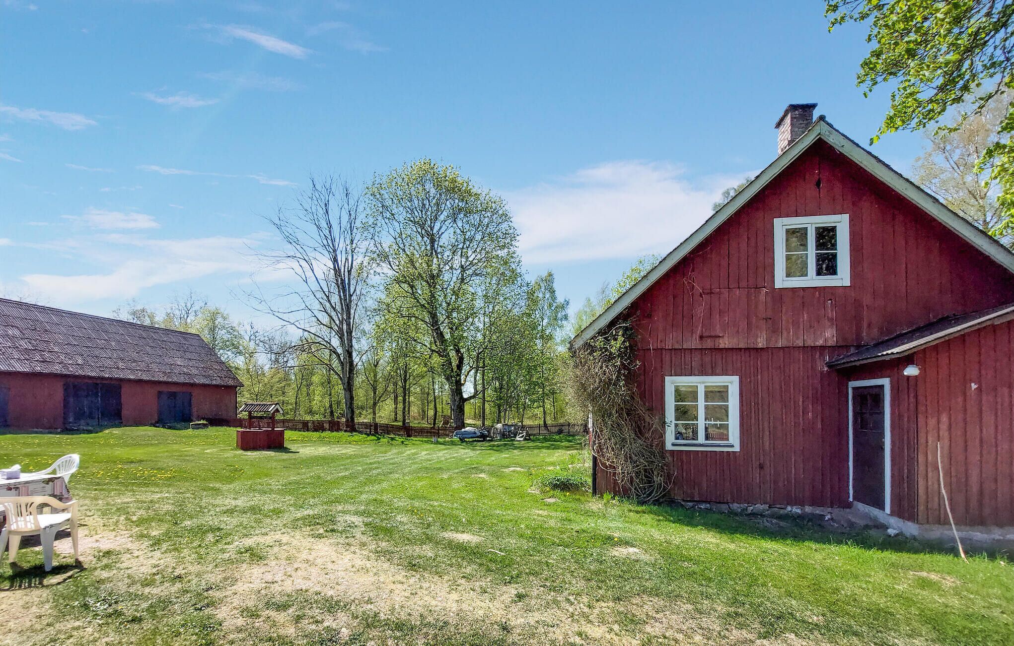 A red barn with a sloped roof and white trim, surrounded by a grassy yard with a few trees and a picnic table.