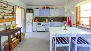 Een kleine keuken met witte kastjes, een eettafel met streepstoelen, en een hanglamp.