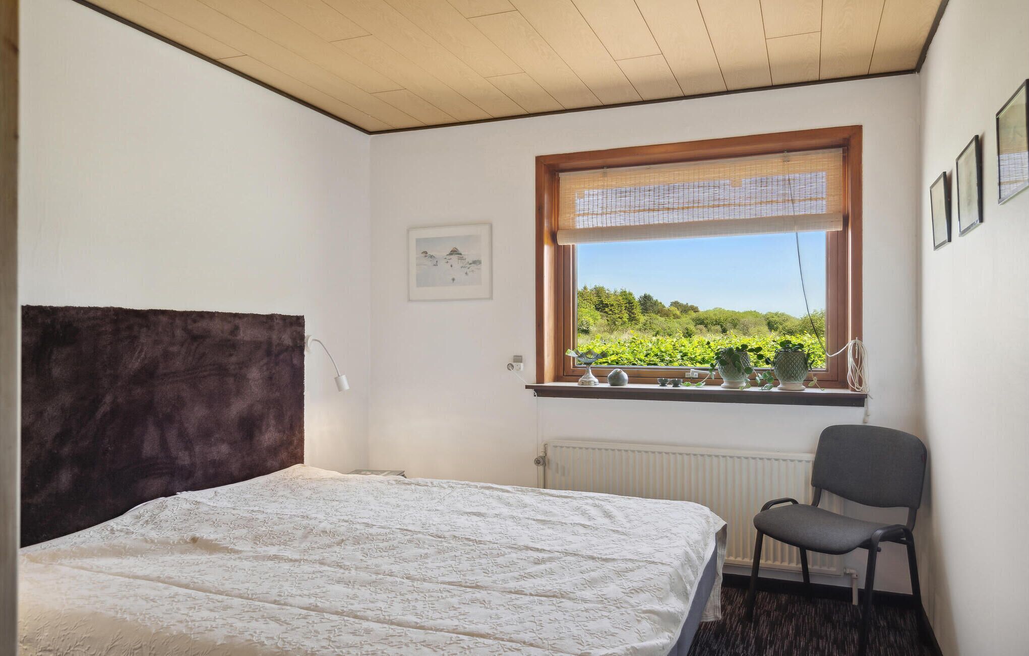 Un dormitorio con cama, una silla, un ventanal con vistas a la vegetación y un radiador.