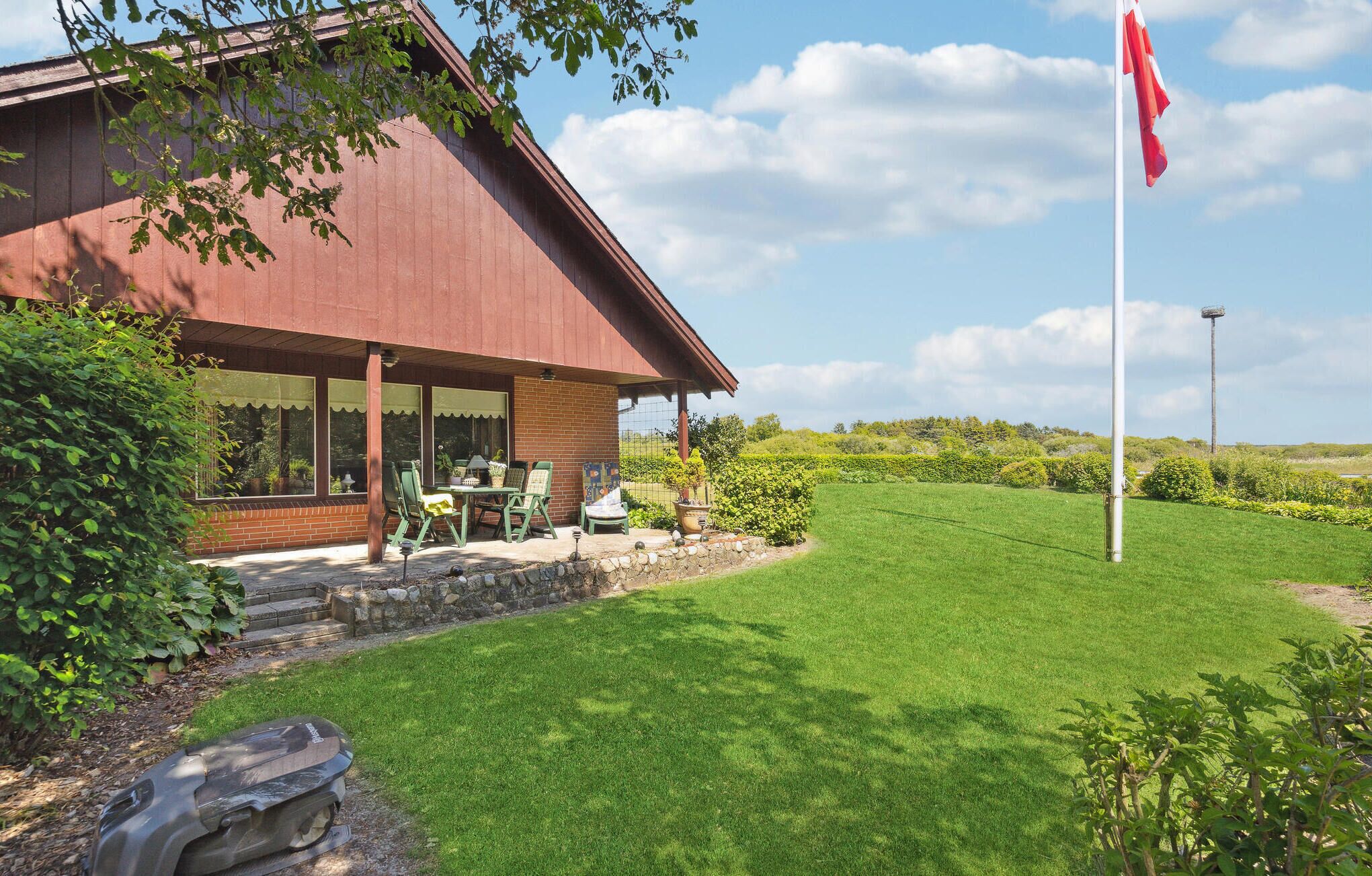 A house with a covered patio, a flag, and a well-maintained lawn.