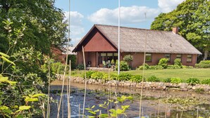 A rustic house with a thatched roof, a stone wall, and a pond in the foreground. - Nice home in Bækmarksbro with WiFi (Bækmarksbro)