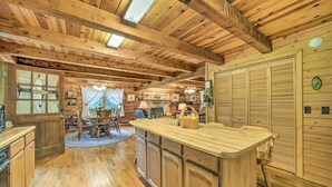 A rustic wooden interior with a kitchen area, wooden cabinets, a dining table, and a bar area. - Scenic Creekside Cabin w/ Wraparound Porch! (Highlands)