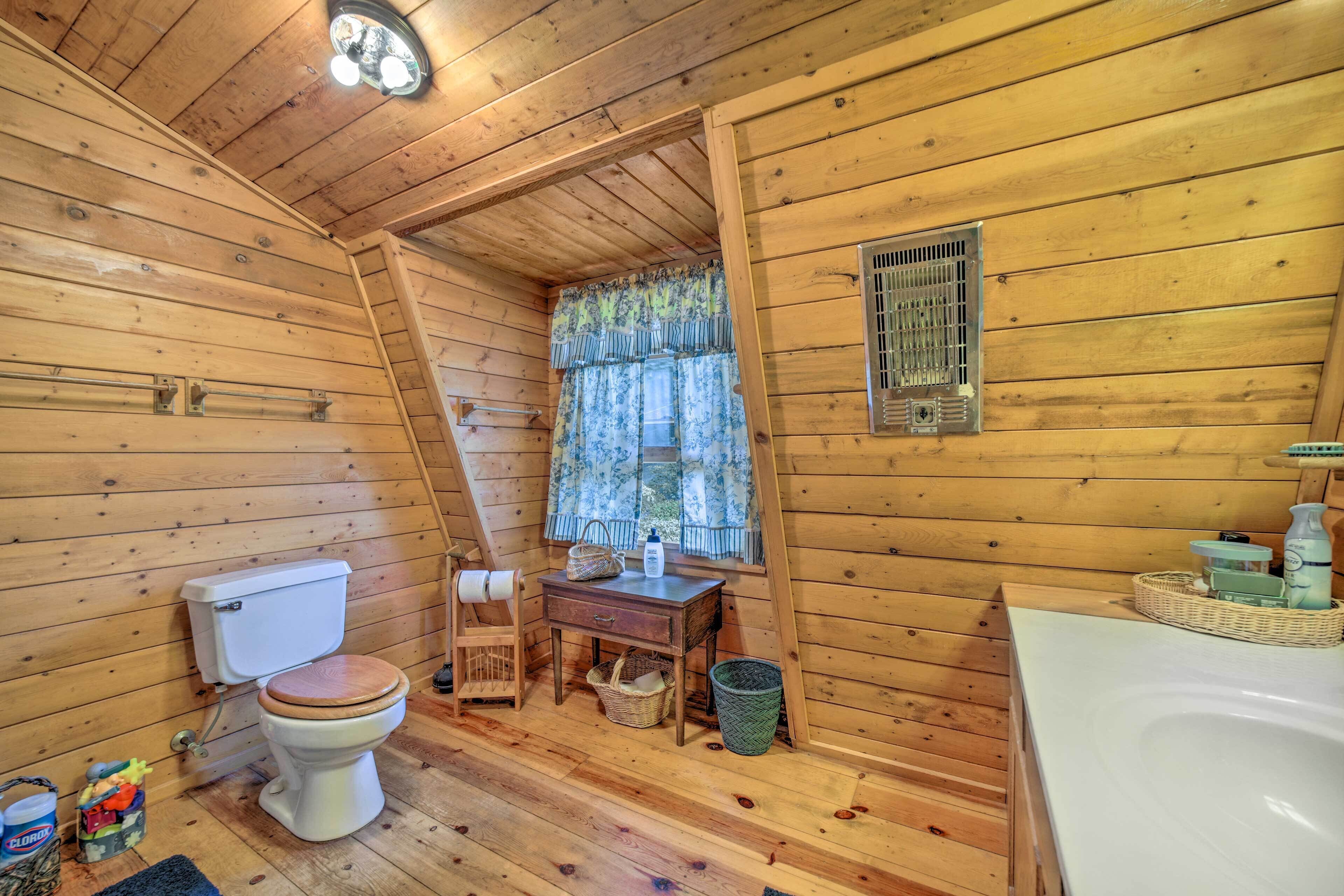 A wooden cabin bathroom with a toilet, sink, and window with curtains.