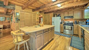 A rustic wooden kitchen with a central island, wooden bar stools, and a built-in oven. - Scenic Creekside Cabin w/ Wraparound Porch! (Highlands)