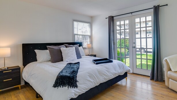 A bedroom with a large bed, a nightstand, a lamp, and a view of the outdoors through a sliding glass door. - Downtown Kirkland Rental: Steps to Lake Washington (Kirkland)