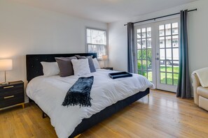 A bedroom with a large bed, a nightstand, a lamp, and a view of the outdoors through a sliding glass door. - Downtown Kirkland Rental: Steps to Lake Washington (Kirkland)