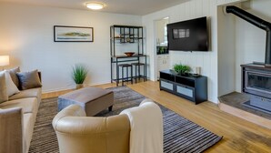 A modern living room with a sofa, ottoman, and a TV mounted on the wall. - Downtown Kirkland Rental: Steps to Lake Washington (Kirkland)