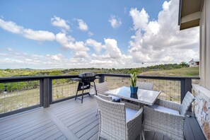 Eine Terrasse mit Grill, Korbmöbeln und einem Tisch mit einem Blumentopf.