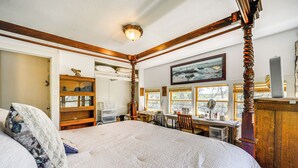 Un dormitorio con una cama grande, cabecera de madera, un escritorio y una silla. Se ve una ventana con vistas a árboles y un cuadro en la pared.