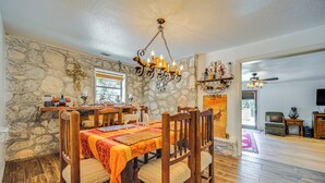Un comedor con pared de piedra, mesa de madera, sillas y una araña.