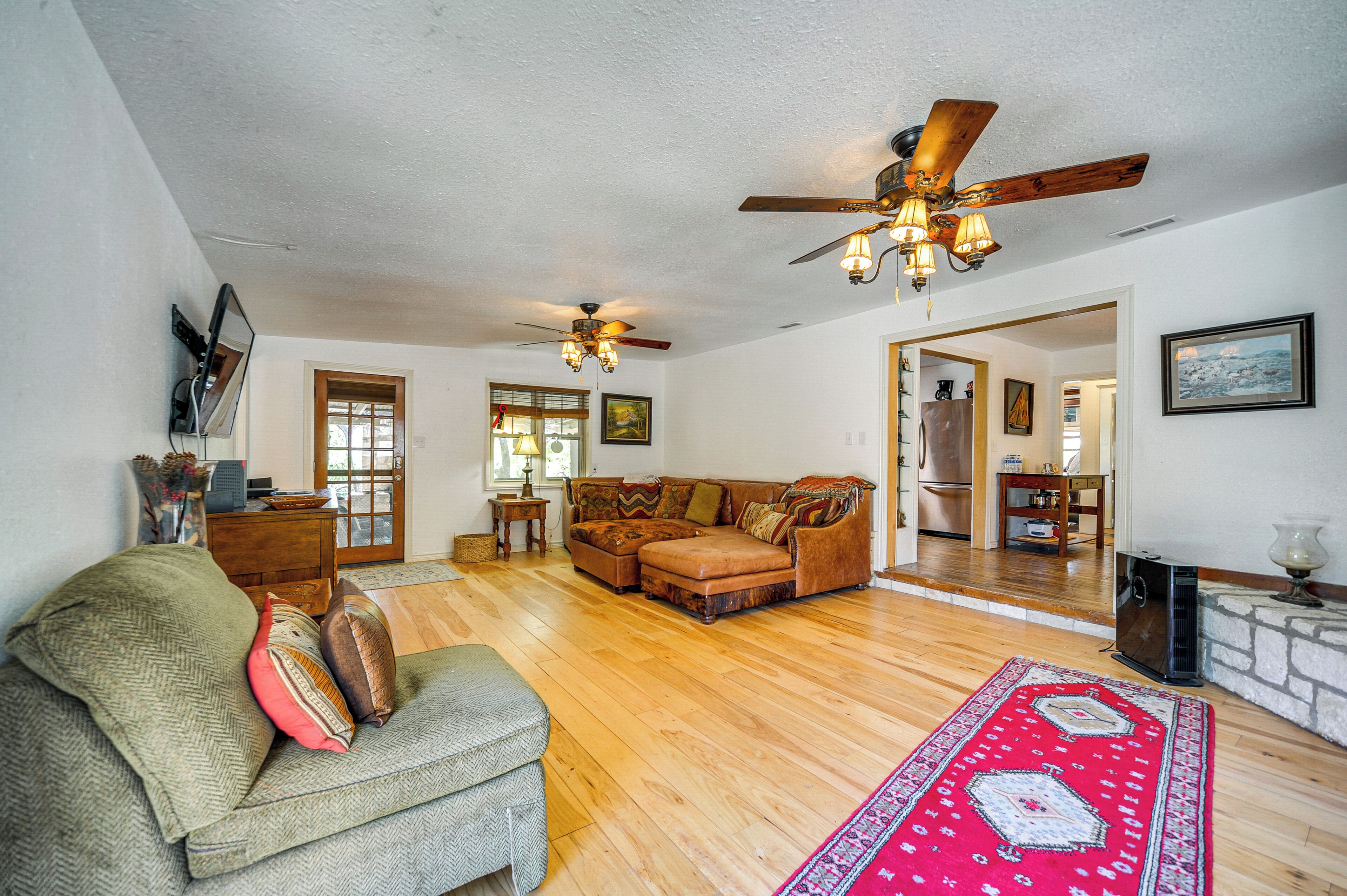 A spacious living room with hardwood flooring, a large sofa, a smaller armchair, and a ceiling fan.