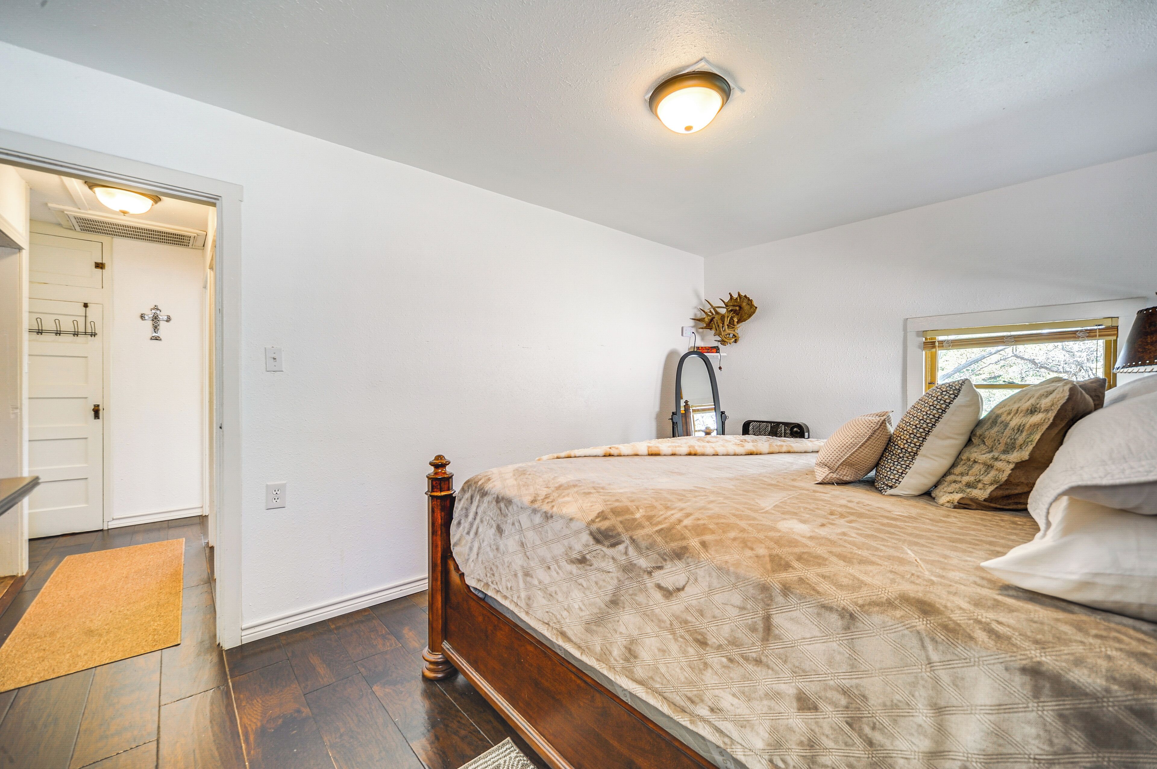 Una camera da letto con un letto di legno, pareti bianche, una finestra e una porta che conduce a un'altra stanza.